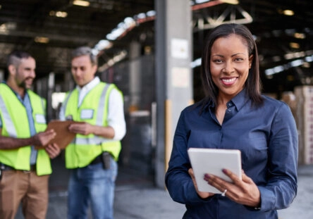 Portrait of a warehouse quality trainier holding a digital tablet with workers in the background