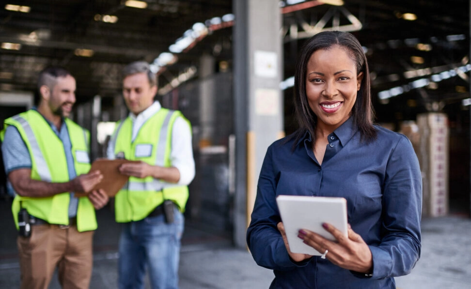 Portrait of a warehouse quality trainier holding a digital tablet with workers in the background